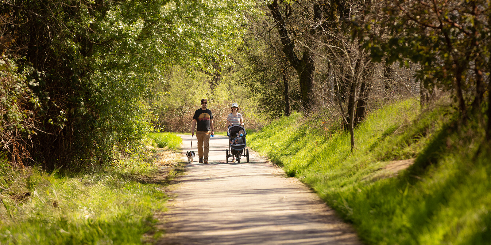 couple walking with dog and stroller on West County Trail