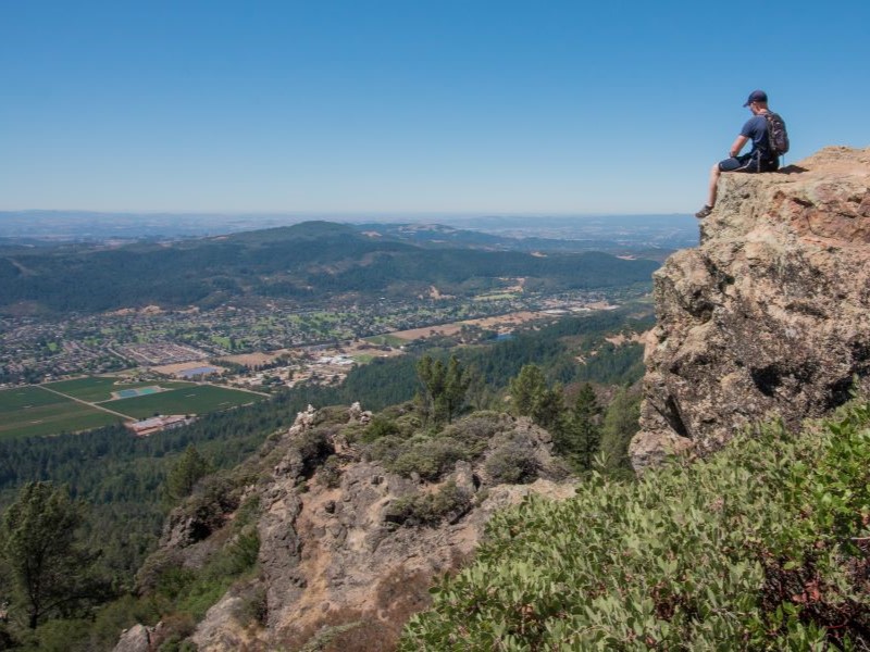 Hiker sits on large rock overlooking valley