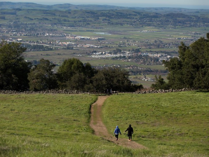 Two hikers on trail with view of valley and city in distance