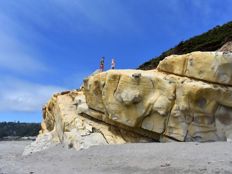Two people stand atop large sandstone rock at Gualala beach